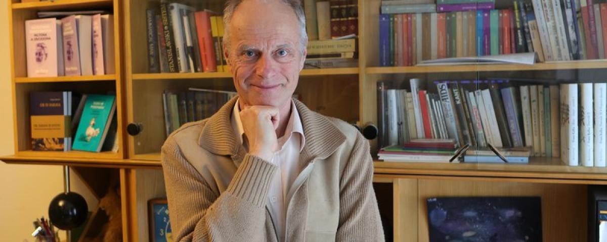 Miran Možina stoji pred knjižno polico 